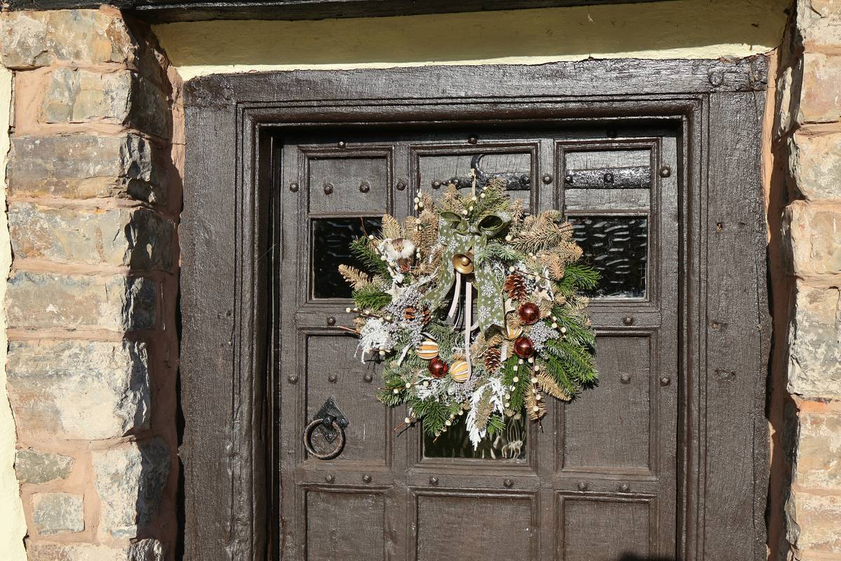 wreaths for christmas decor hanging on a well-painted wooden front door with natural greenery, red ribbon, and pinecones